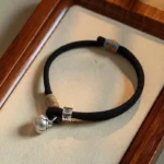 Tibetan red string bracelet with silver om mani padme hum charm and persimmon bell on wooden tray