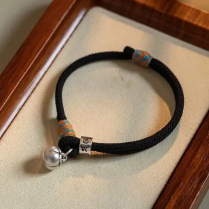 Tibetan red string bracelet with silver om mani padme hum charm and persimmon bell on wooden tray