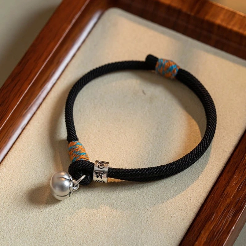 Tibetan red string bracelet with silver om mani padme hum charm and persimmon bell on wooden tray