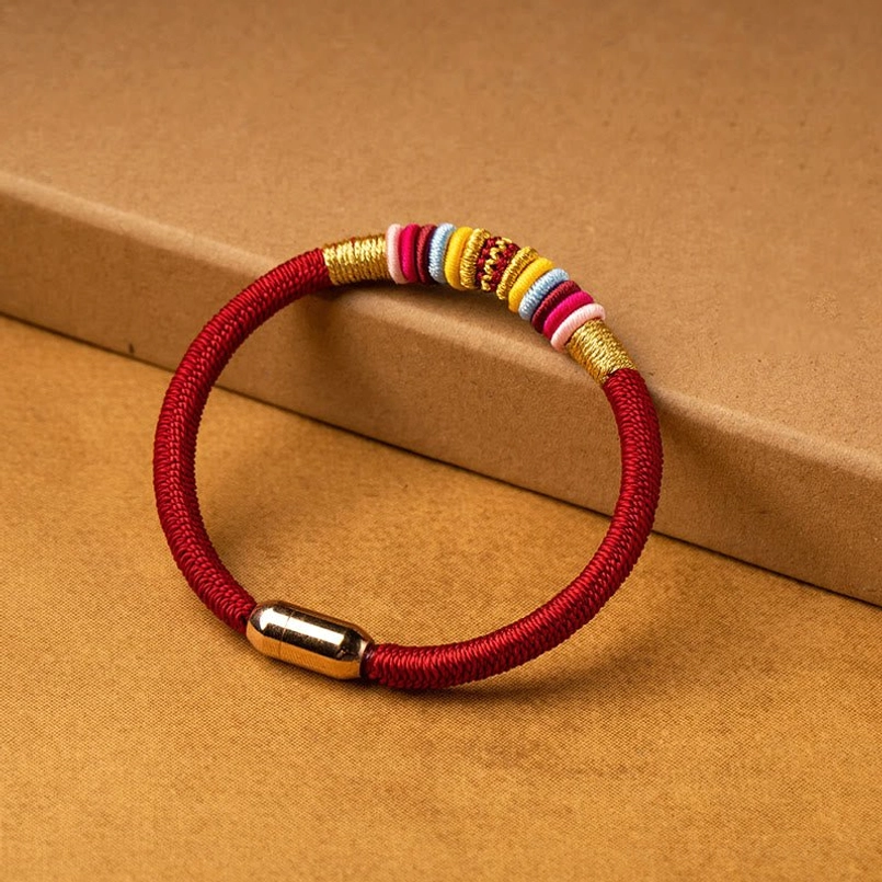 Red braided Tibetan protection bracelet with gold magnetic clasp side view on kraft paper