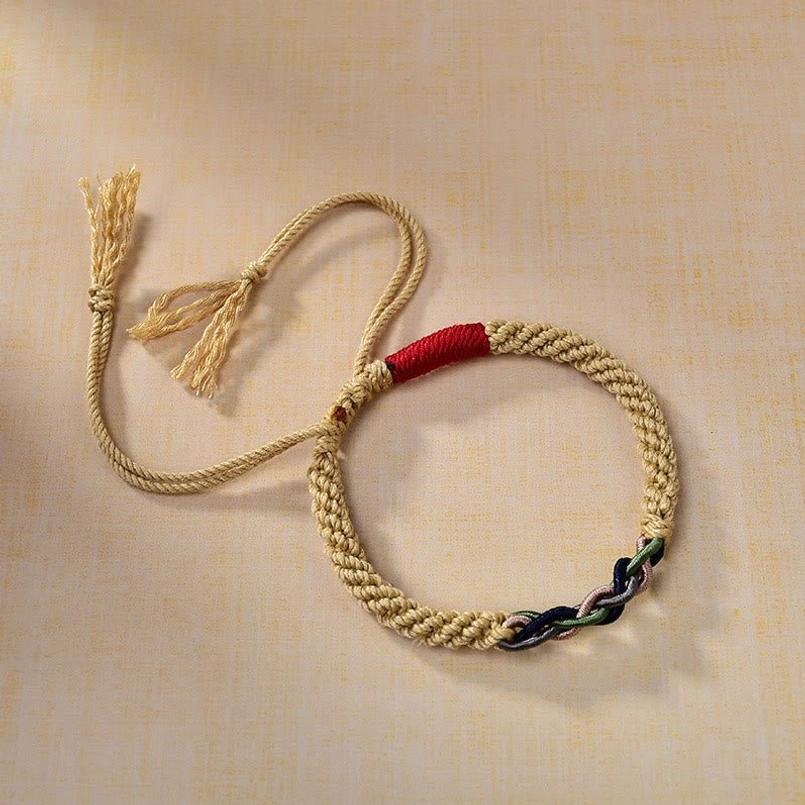 Three-quarter view of authentic Tibetan red string luck bracelet showing beige braided rope, red protection cord, and multiple tassel details