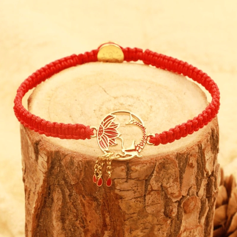 Tibetan red string lucky bracelet with gold metal charm on wooden display - side view