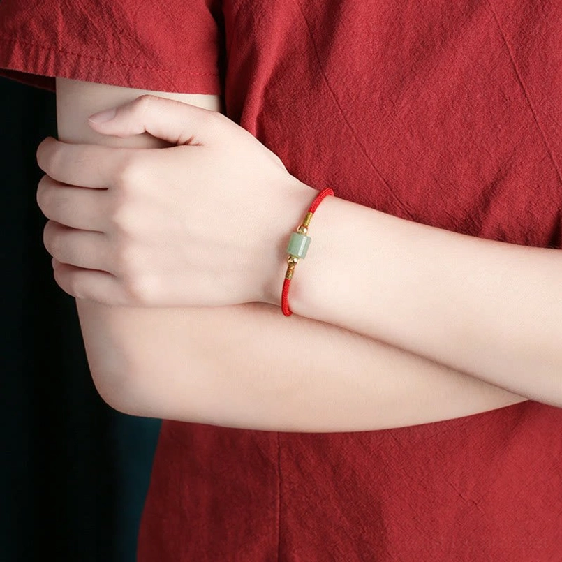 Woven red string protection bracelet worn on wrist with green aventurine stone bead detail