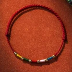 Hand-woven Tibetan red string protection bracelet with multicolor beads and copper alloy spacers, adjustable cord design on leather background