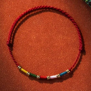 Hand-woven Tibetan red string protection bracelet with multicolor beads and copper alloy spacers, adjustable cord design on leather background