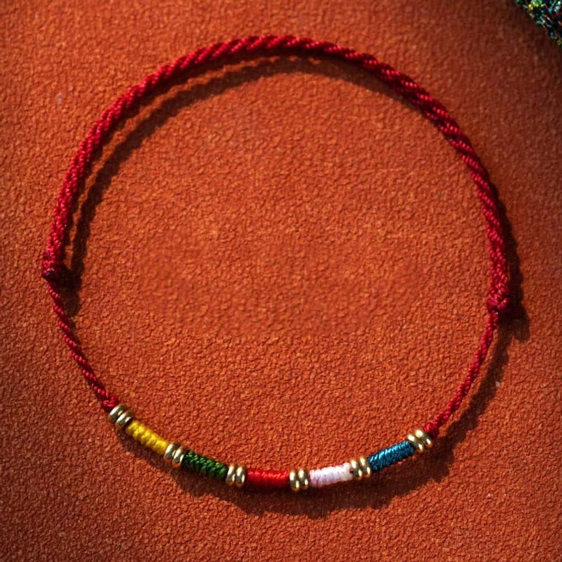Hand-woven Tibetan red string protection bracelet with multicolor beads and copper alloy spacers, adjustable cord design on leather background