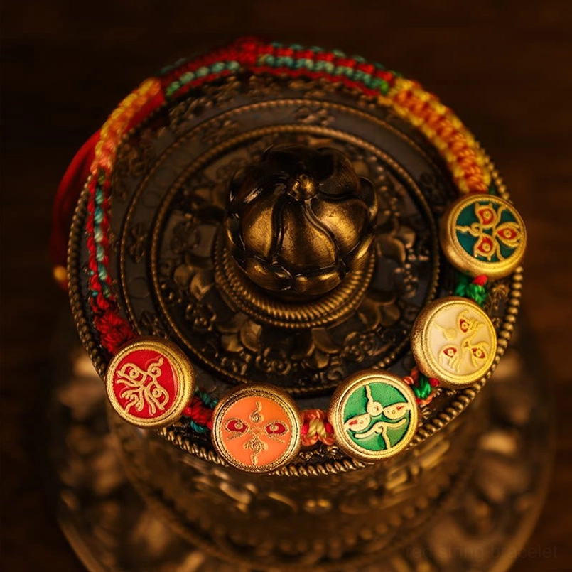 Five Gods of Wealth Tibetan luck bracelet high-angle view with gold-framed enamel pendants in Tibetan-style container