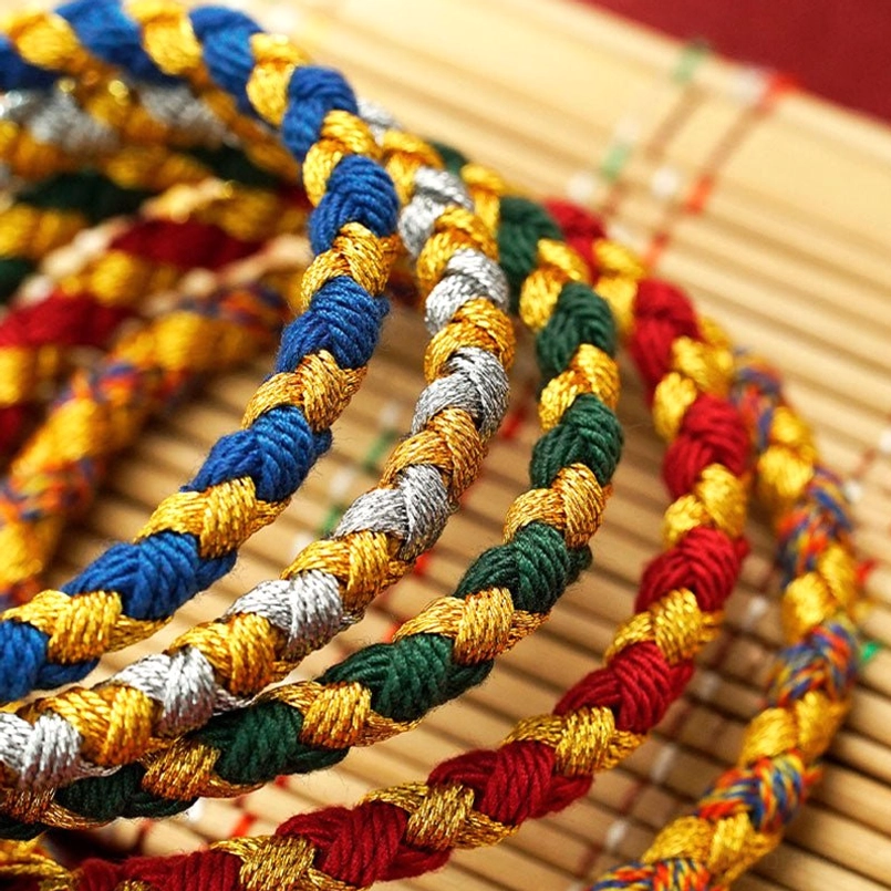 Coiled tibetan woven luck bracelets in mixed colors neatly arranged on bamboo desktop