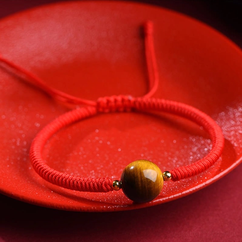 Tiger eye red string bracelet with single bead on ceramic plate background detail view