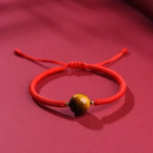 Tiger eye red string bracelet with single 10mm bead and gold spacers on red fabric background