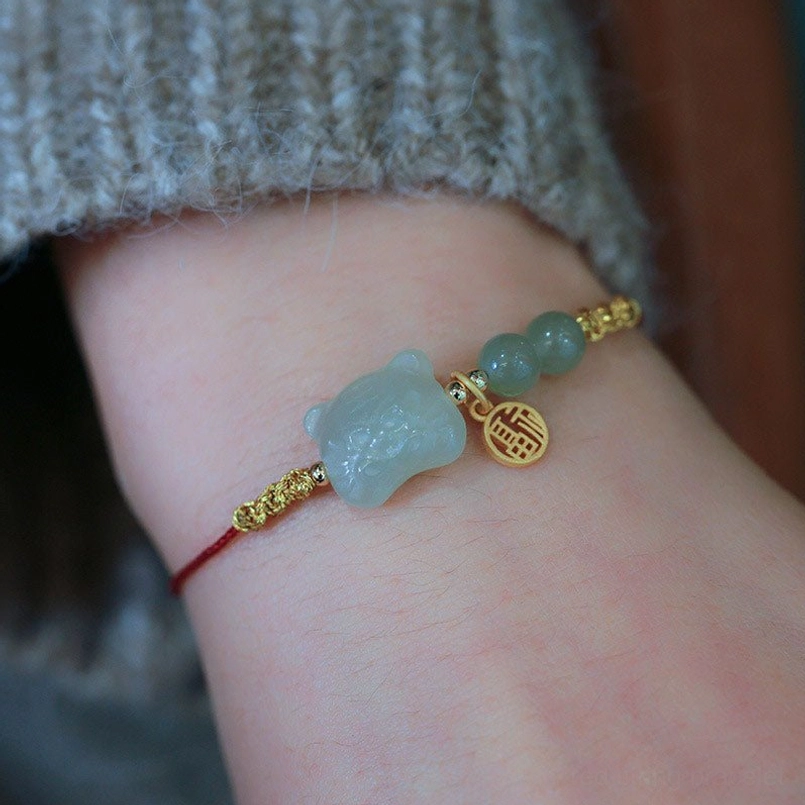 Chinese zodiac tiger jade red string bracelet close-up showing large jade tiger charm and round fu pendant with red cord