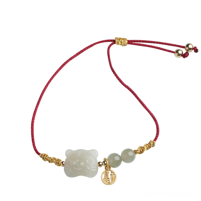 Chinese zodiac tiger jade red string bracelet flat lay showing adjustable woven red cord, jade tiger charm and gold hardware