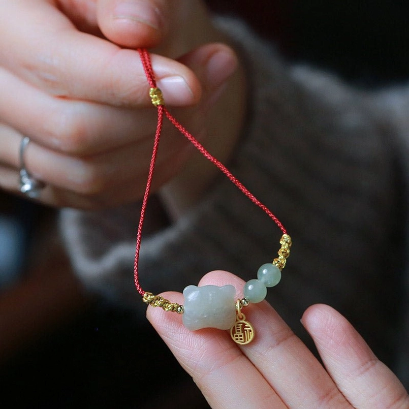 Chinese zodiac tiger jade red string bracelet with fu pendant held in hand showing jade beads and gold accents
