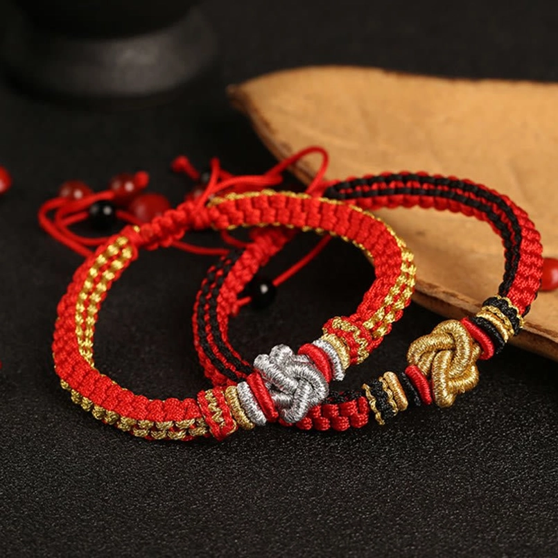 Multiple handmade red black and gold woven lucky bracelets with silver knot on black table
