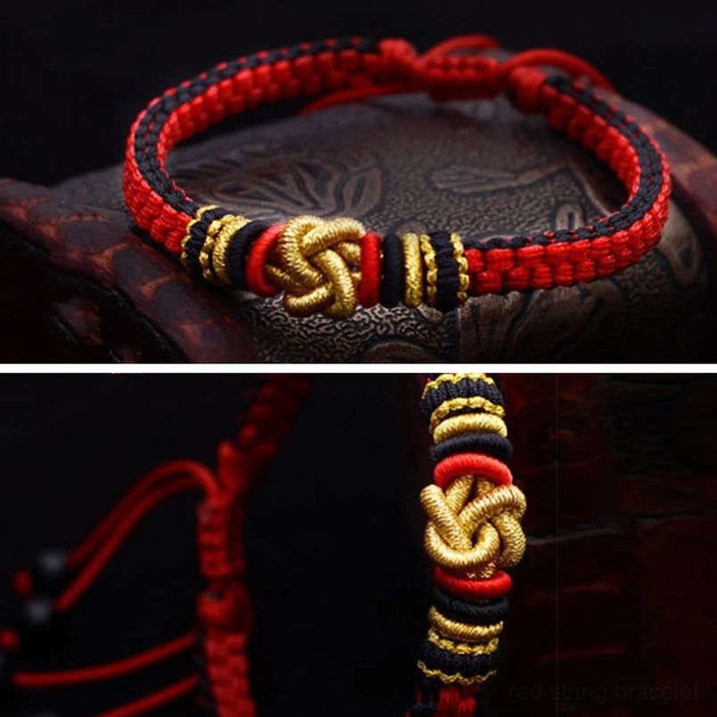 Single red black and gold handmade lucky bracelet with golden knot on wooden background