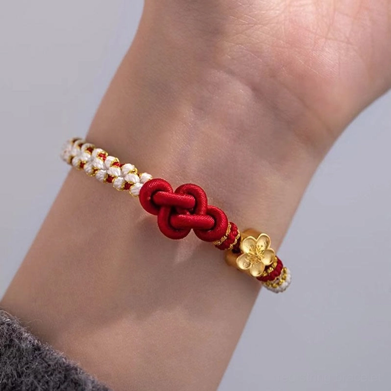 Red string love knot bracelet worn on wrist with gold flower decoration and beaded trim detail