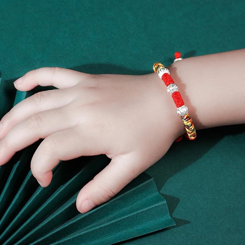 Children's twisted red rope King Kong knot bracelet with mixed metal silver beads on child's wrist, top-side angle
