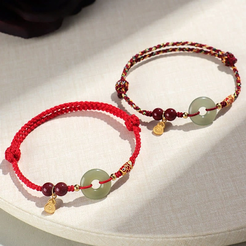 Two Hetian Jade Peace Buckle red and black string bracelets on linen background