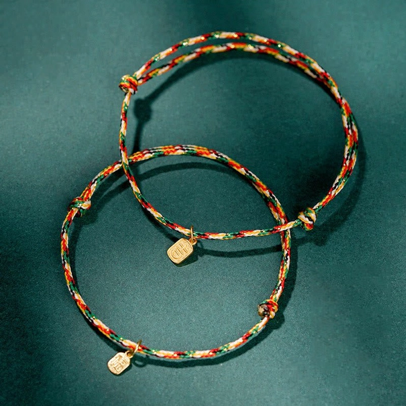 Two multicolor braided Fu character lucky red string bracelets on dark green background