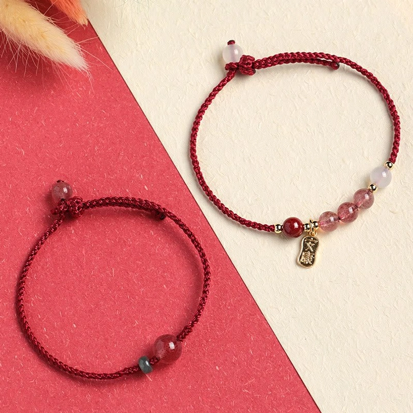 Two red string bracelets with strawberry quartz and gemstone charms on red beige background