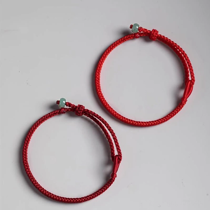 Two minimalist red string jade bracelets flat lay on light gray background