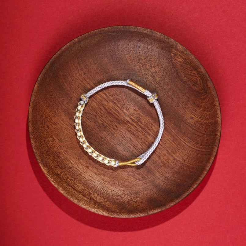 Two-tone thin woven red string bracelet with gold threads on wooden plate
