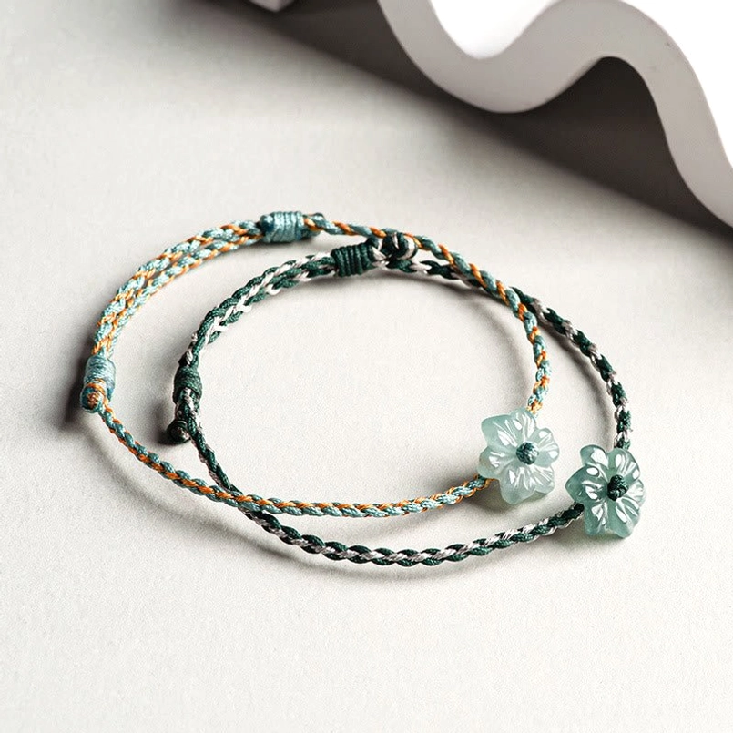 Flat lay of two jade orchid braided bracelet variants on decorative wavy background