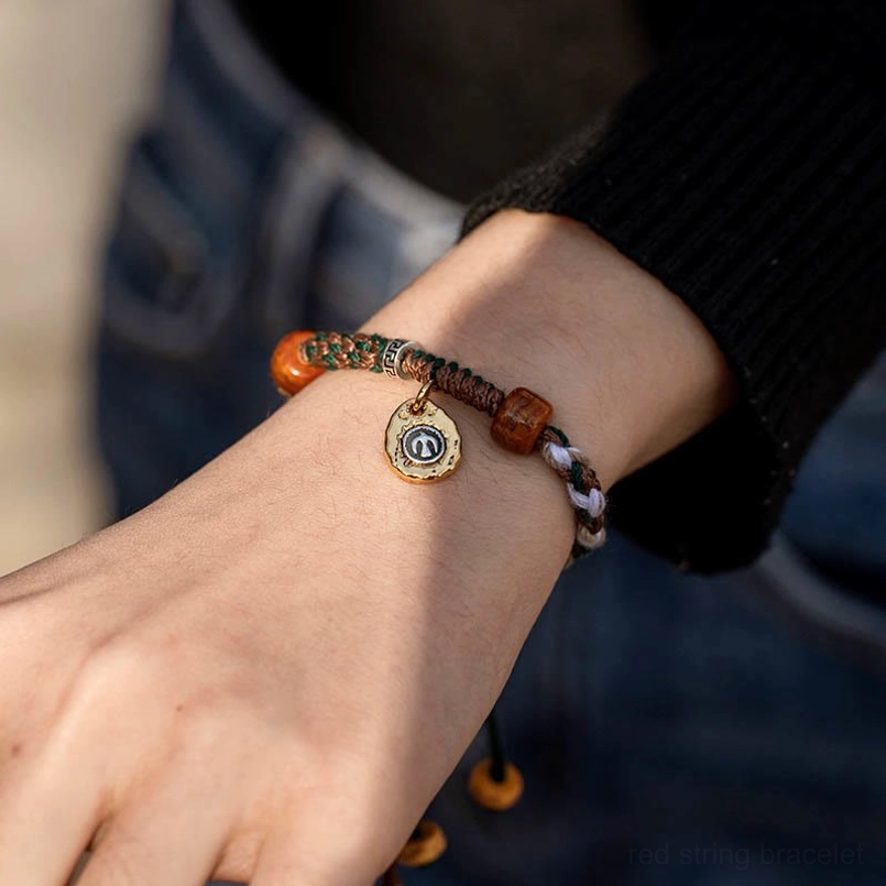 Tibetan red string bracelet worn on wrist with black sleeve and denim background