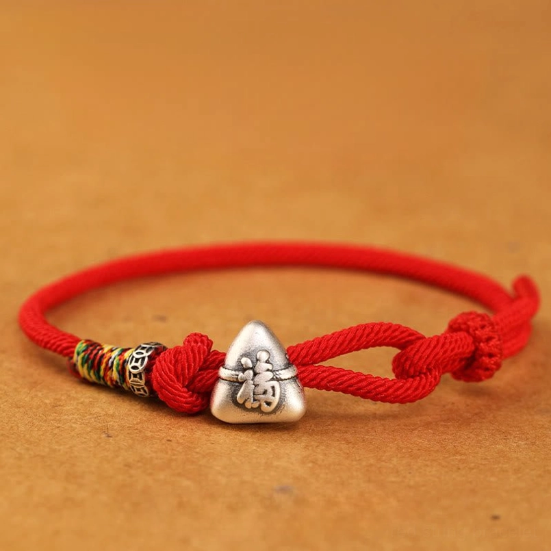 Vibrant red fu zongzi red string bracelet flat lay on brown background