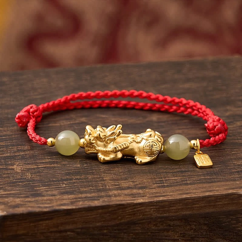 Top down flat lay of Pi Xiu red string bracelet on dark wood tabletop