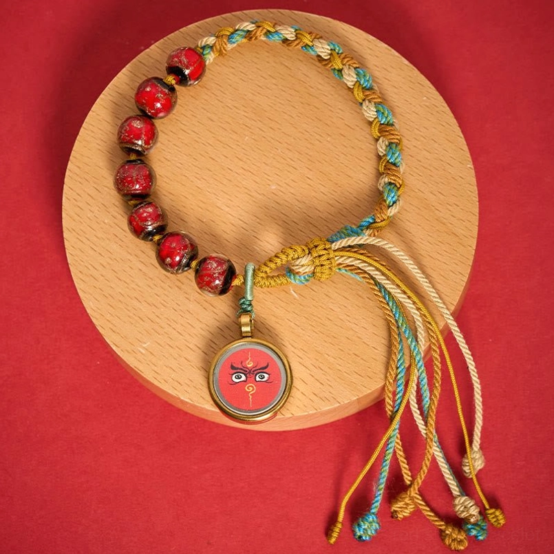 Red Five Directions Wealth God Buddha Eye bracelet with gold-framed pendant, flat lay display
