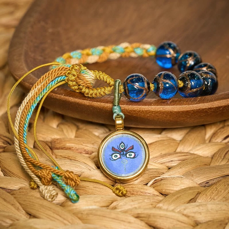 Tibetan liuli glass bead bracelet with Buddha eye pendant and braided cord, low angle view on straw mat