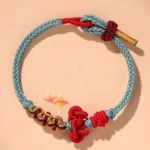 Wenchang knot red string bracelet overhead view with light sky blue braided cord and red Chinese knot on peach background