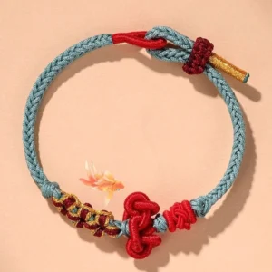 Wenchang knot red string bracelet overhead view with light sky blue braided cord and red Chinese knot on peach background