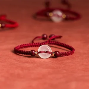 White agate peace buckle red string bracelet side overhead view on red textile tabletop