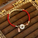 White jade fu character red string blessing bracelet on vintage gold-trimmed velvet, top view with peace buckle detail