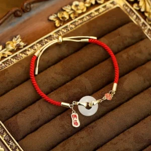White jade fu character red string blessing bracelet on vintage gold-trimmed velvet, top view with peace buckle detail