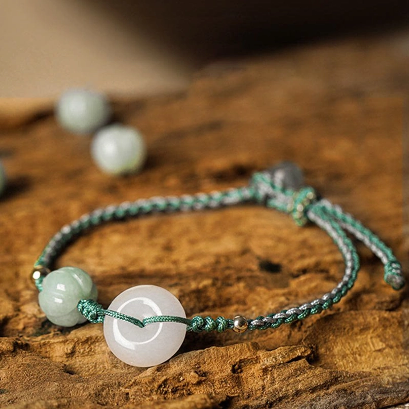 White jade peace buckle braided bracelet with green pumpkin bead on natural wooden surface