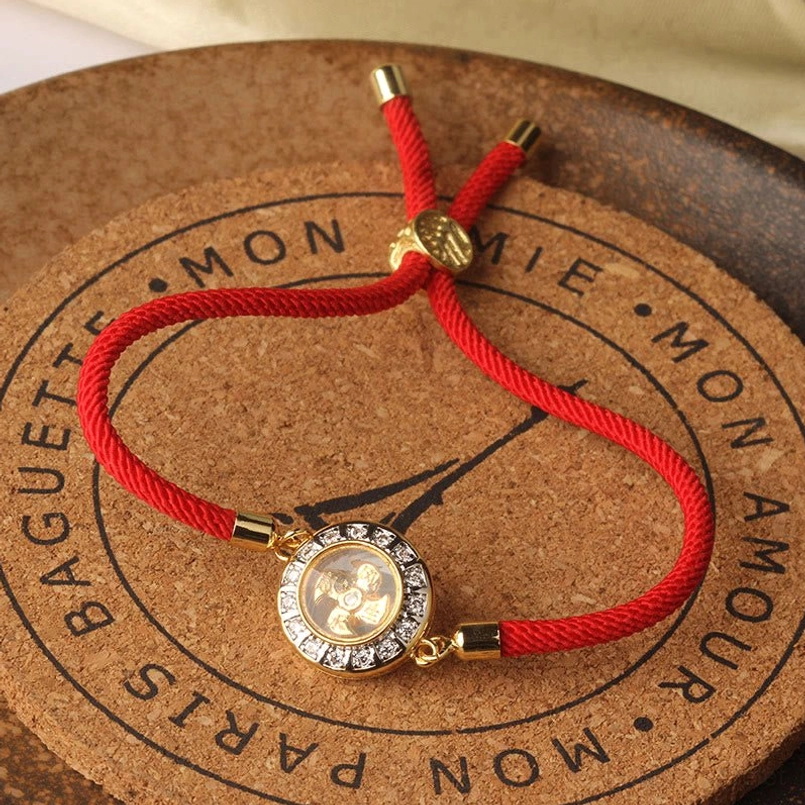 Feng shui red string windmill bracelet displayed on cork coaster, full product view