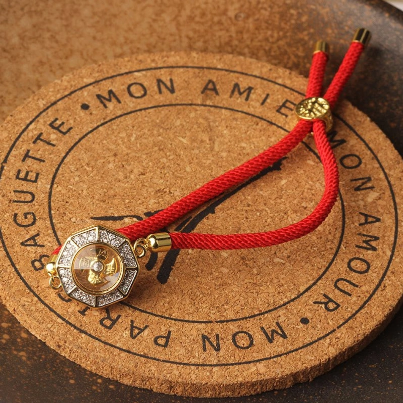 Close-up overhead view of rotatable octagonal copper windmill charm with red braided rope and polished metal fittings