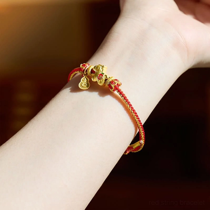 Red string copper bracelet worn on wrist showing dangling gold horse and gourd charms