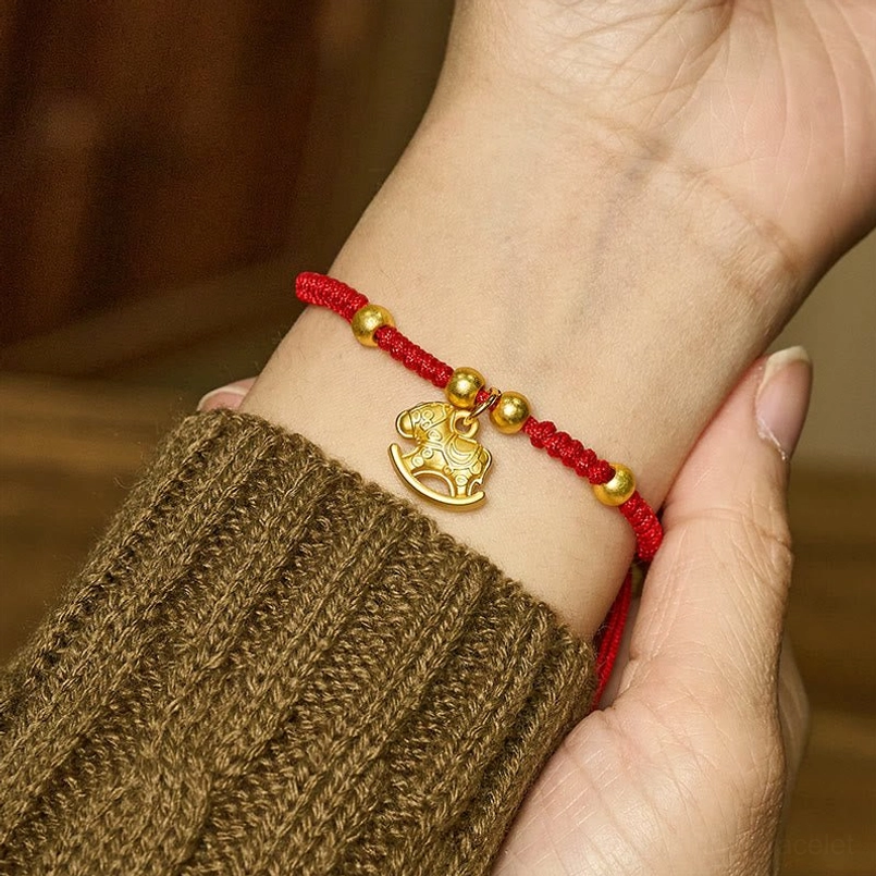 Red string rocking horse bracelet worn on wrist with knitted sweater sleeve, close-up side view