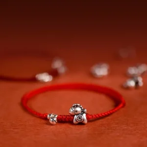 Year of the Horse sterling silver red string bracelet with bell charm close-up detail on reddish fabric background