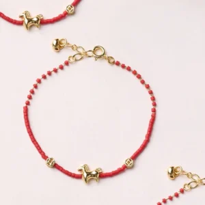 Year of the Horse red liuli glass bracelet with gold-plated horse charm and coin accent on neutral tabletop