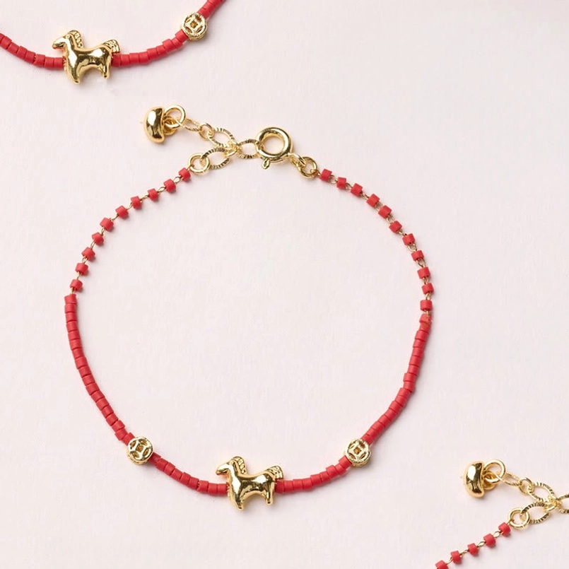 Year of the Horse red liuli glass bracelet with gold-plated horse charm and coin accent on neutral tabletop