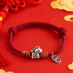 Year of the Horse red string bracelet with 999 sterling silver Fu charm on festive red gold backdrop