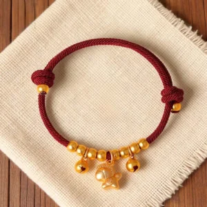 Year of the Horse red string bracelet with gold horse charm and bells, adjustable lucky cord, top view flat lay on linen