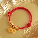 Year of the Horse red string bracelet with gold rocking horse charm on gilded cloud tabletop