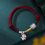 Year of the Horse sterling silver red string bracelet with engraved silver barrel and horse charm on dark green background