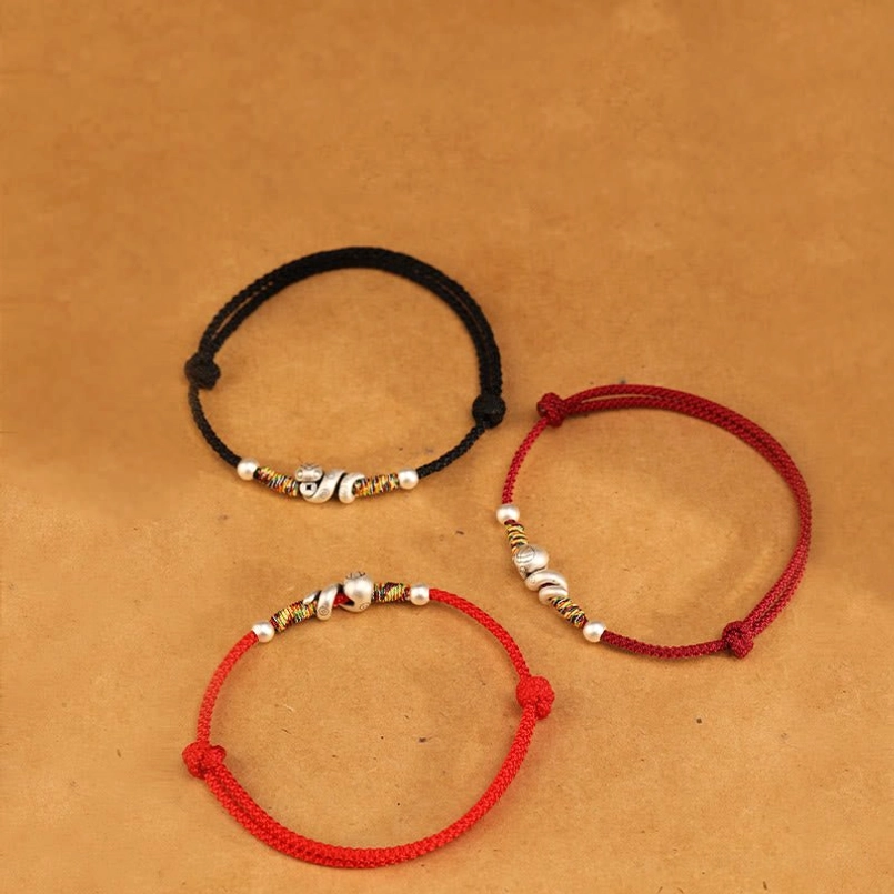 Flat lay display of Year of the Snake anklet style options in red and black cord with silver decorative snake charms